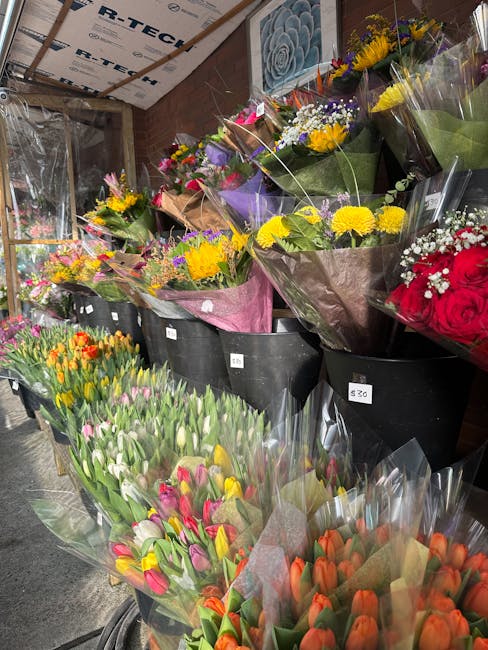 A display of vibrant flower bouquets arranged on black containers in a flower shop setting. The bouquets include an assortment of fresh flowers such as bright yellow chrysanthemums, pink tulips, orang